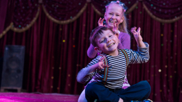 Two funny playful children, boy and girl, smiling while acting as monsters with claws, on a purple stage, in a theatrical representation