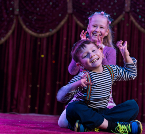 Two funny playful children, boy and girl, smiling while acting as monsters with claws, on a purple stage, in a theatrical representation